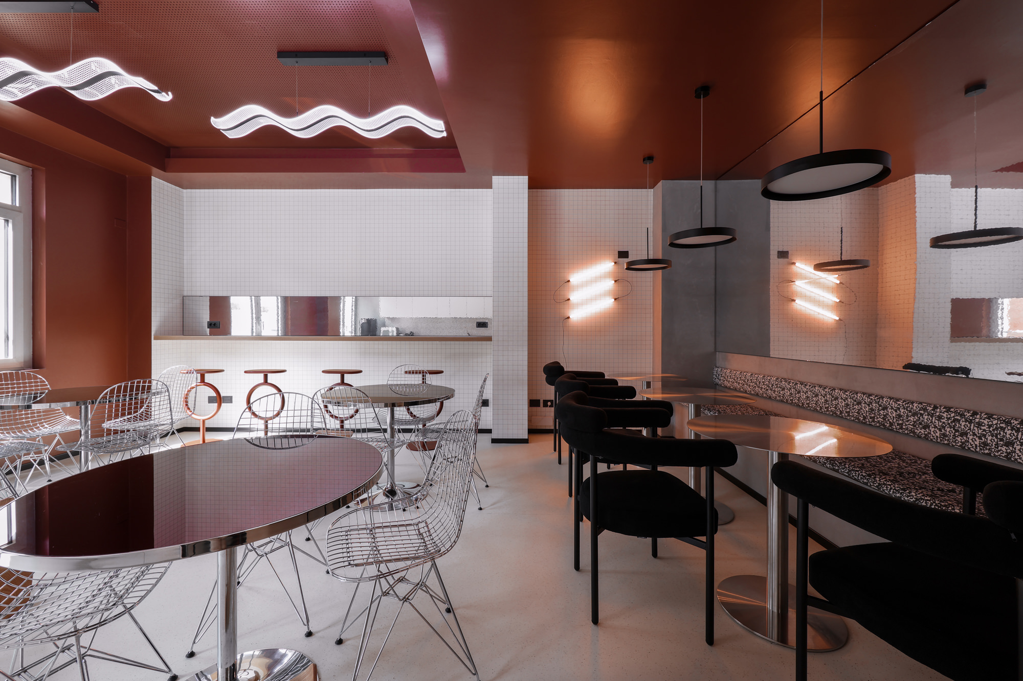 Cucina ampliata di Pattari Headquarters a Milano, con tavoli metallici, sedie Vitra, sgabelli Sancal, illuminazione scultorea e soffitto rosso.
